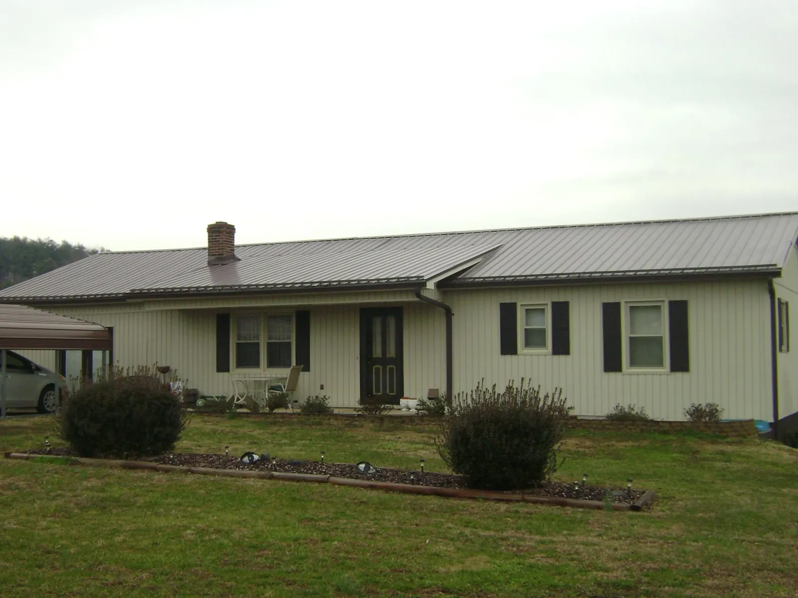 Brown metal roof on a cream sided ranch home with a brick chimney in White Plains