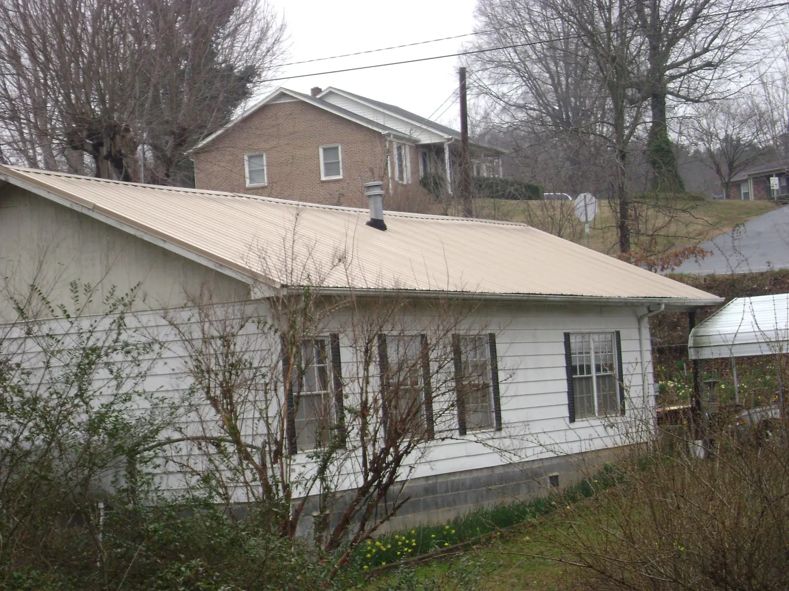 Tan metal roof on a white sided house set into a hillside — Commercial Roofing by Roofing Brothers in White Plains